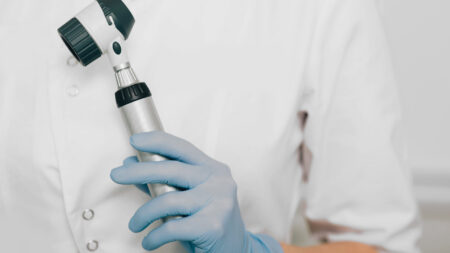 Hand in blauen Handschuhen hält ein Otoskop.