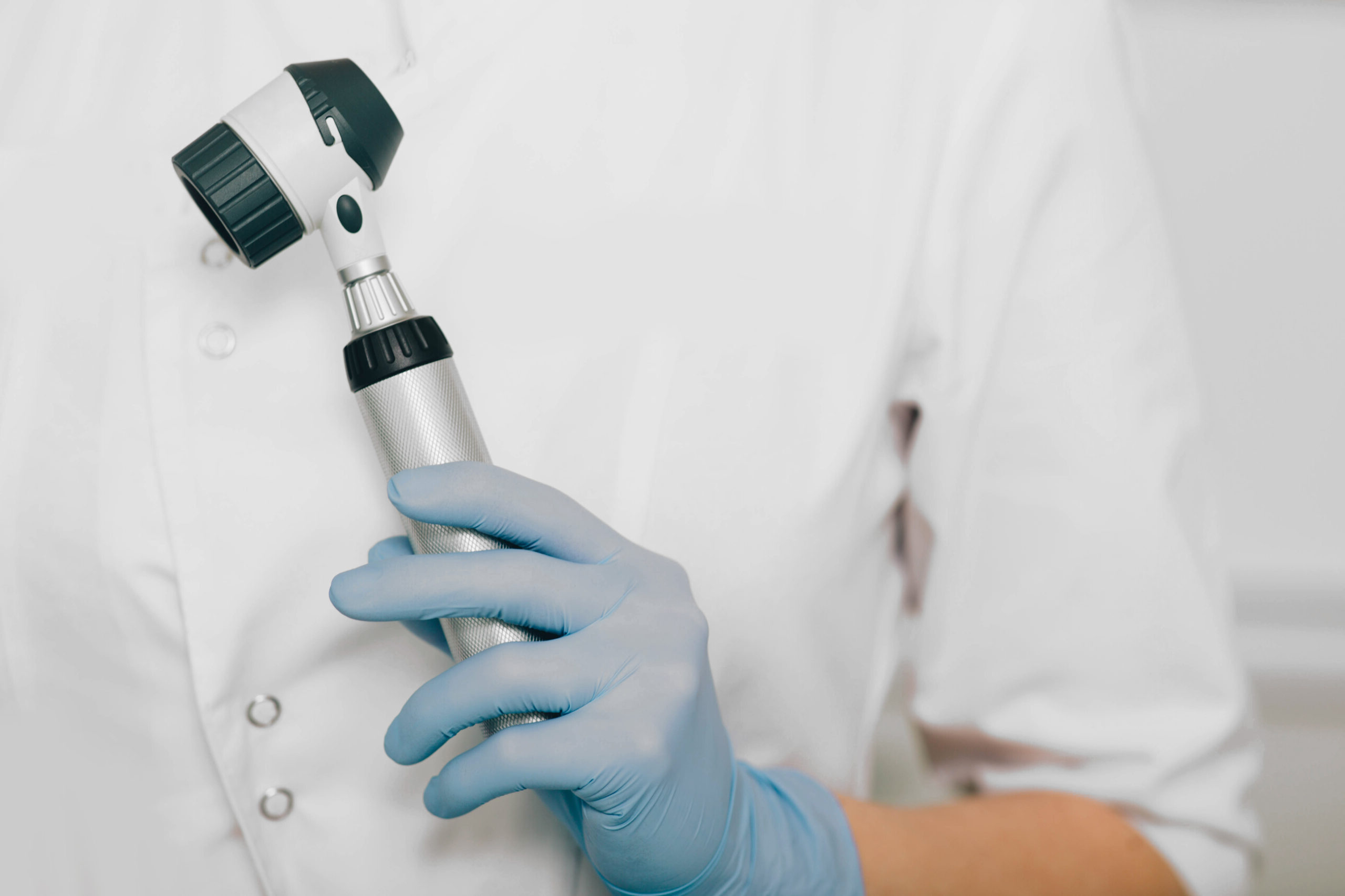 dermatologist with dermatoscope, close-up hand with dermatoscope Hand in blauen Handschuhen hält ein Otoskop.