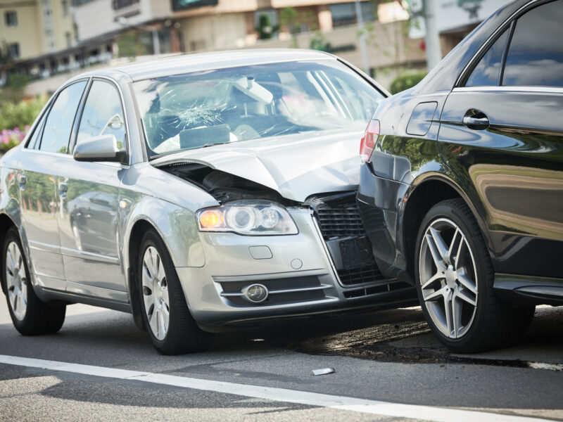 Frontale Kollision zwischen einem silbernen und einem schwarzen Auto auf einer Straße, mit sichtbaren Schäden an beiden Fahrzeugen.